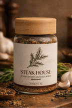 Jar of 'Steak House' seasoning on a wooden cutting board with herbs and garlic.